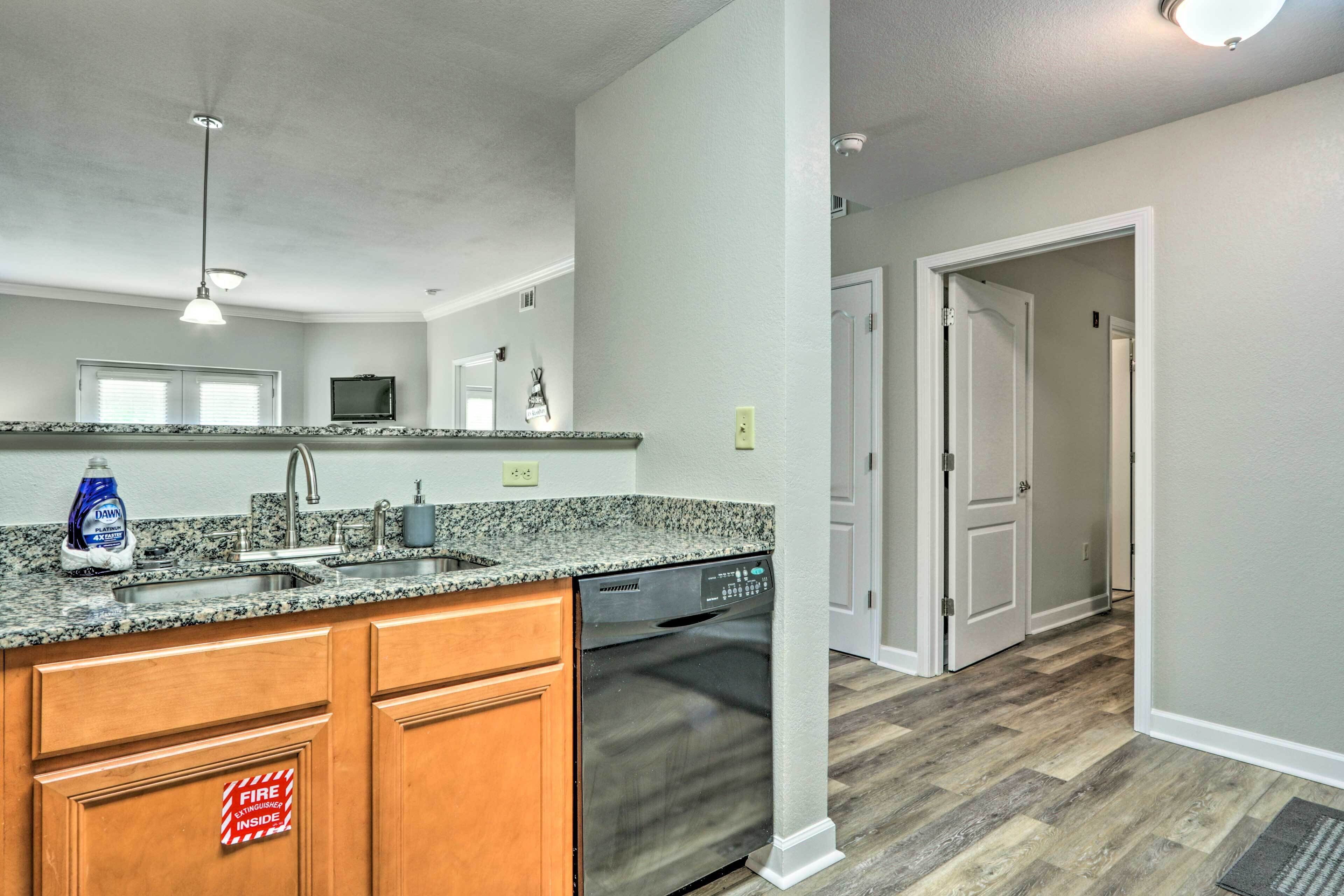 A kitchen with granite countertops, wooden cabinets, a dishwasher, and a fire safety sign.