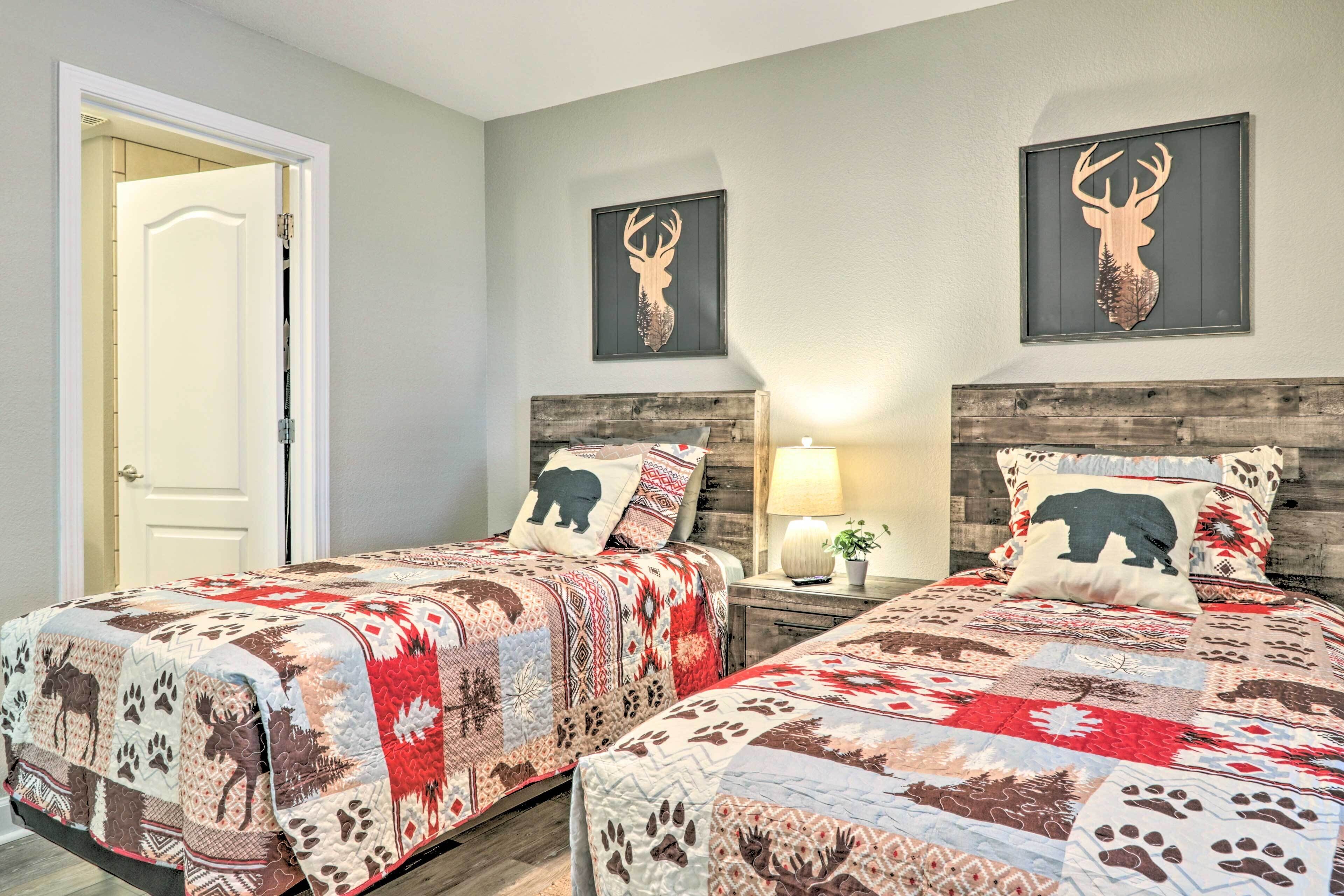 A bedroom with two beds, each with a patterned quilt and a pillow featuring a deer head.