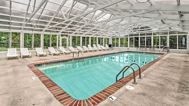 An indoor swimming pool with a glass ceiling, surrounded by white lounge chairs and a brick border. - Community Pool Access! Dtwn Pigeon Forge Condo (Pigeon Forge)