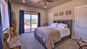 A bedroom with a bed, a ceiling fan, a view through the window, and a door. - Quiet Kanab Home w/ Panoramic Views & Porch! (Kanab)