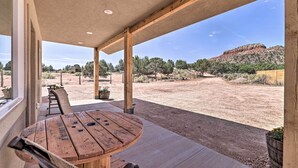 A covered patio with a wooden table and chairs, overlooking a desert landscape with sparse vegetation and distant hills. - Quiet Kanab Home w/ Panoramic Views & Porch! (Kanab)