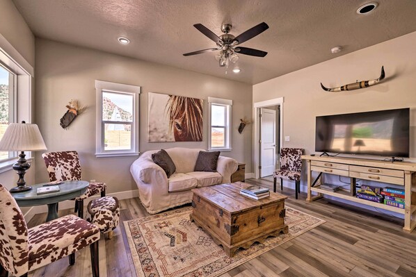 A living room with a sofa, chairs, a coffee table, a TV stand, and a ceiling fan. - Quiet Kanab Home w/ Panoramic Views & Porch! (Kanab)