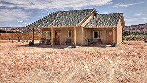 A two-story house with a sloped roof, a covered patio, and a dirt yard. - Quiet Kanab Home w/ Panoramic Views & Porch! (Kanab)