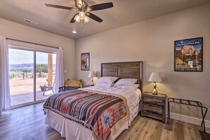 A bedroom with a large bed, a ceiling fan, a nightstand with a lamp, and a poster on the wall. - Quiet Kanab Home w/ Panoramic Views & Porch! (Kanab)
