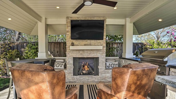 Une terrasse extérieure avec une cheminée en pierre, deux fauteuils en cuir et un barbecue.