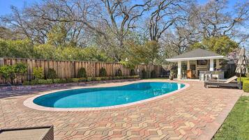 A backyard with a swimming pool, a gazebo, and a wooden fence.