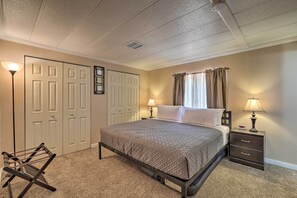 A bedroom with a bed, two bedside tables with lamps, a nightstand, a wall-mounted clock, and a folding chair.