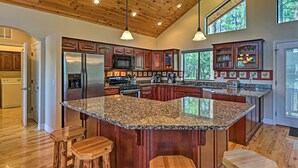 A spacious kitchen with granite countertops, wooden cabinets, and a large island with stools. - Serene Lakeside Cabin w/ Decks + Edler Lake Views! (Pinetop)