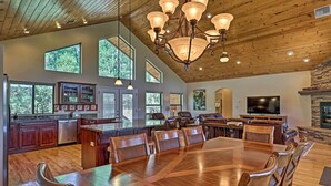 A spacious kitchen with a large island, wooden dining table, and chairs. There are multiple windows providing natural light and views of the outdoors. - Serene Lakeside Cabin w/ Decks + Edler Lake Views! (Pinetop)
