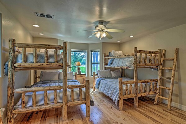 A room with bunk beds made of wood, a ceiling fan, and a window with a view of greenery.