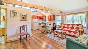 A spacious living room with a wooden floor, a red and white quilted sofa, a green armchair, and a dining area with a table and chairs. - Cozy Tannersville Gem - Ski, Hike, Explore! (Tannersville)