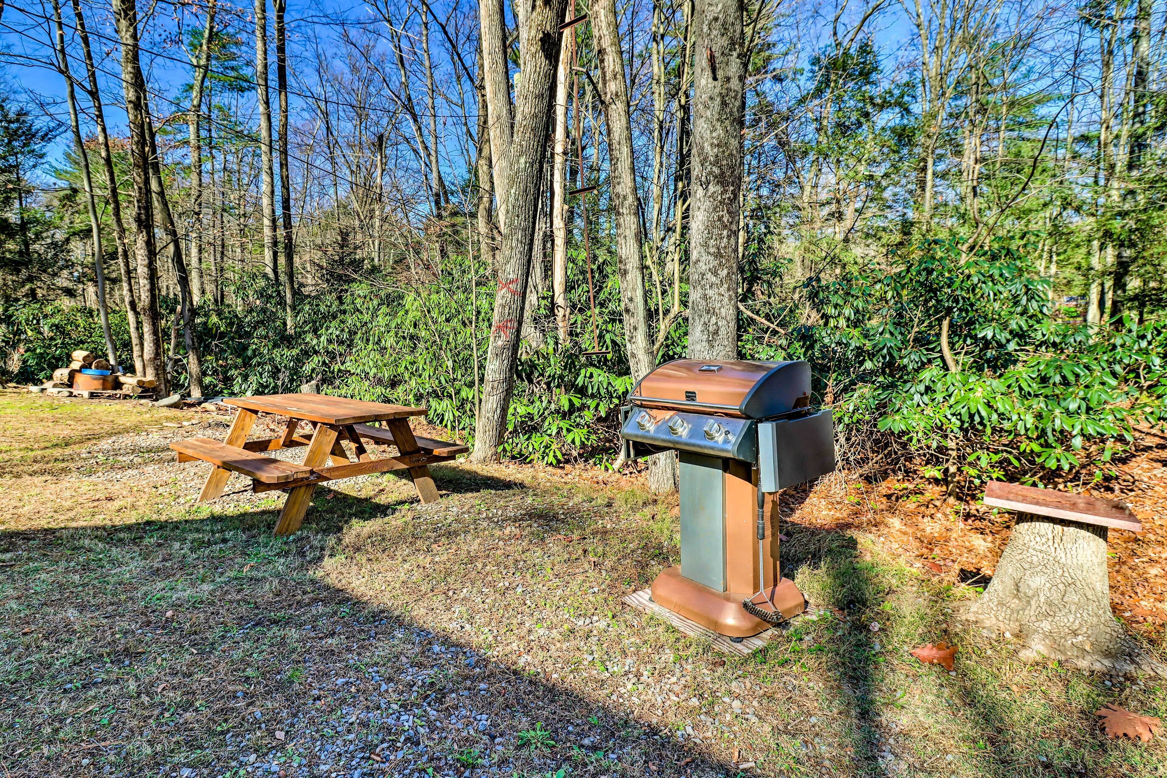 A picnic table and a barbecue grill in a wooded area.