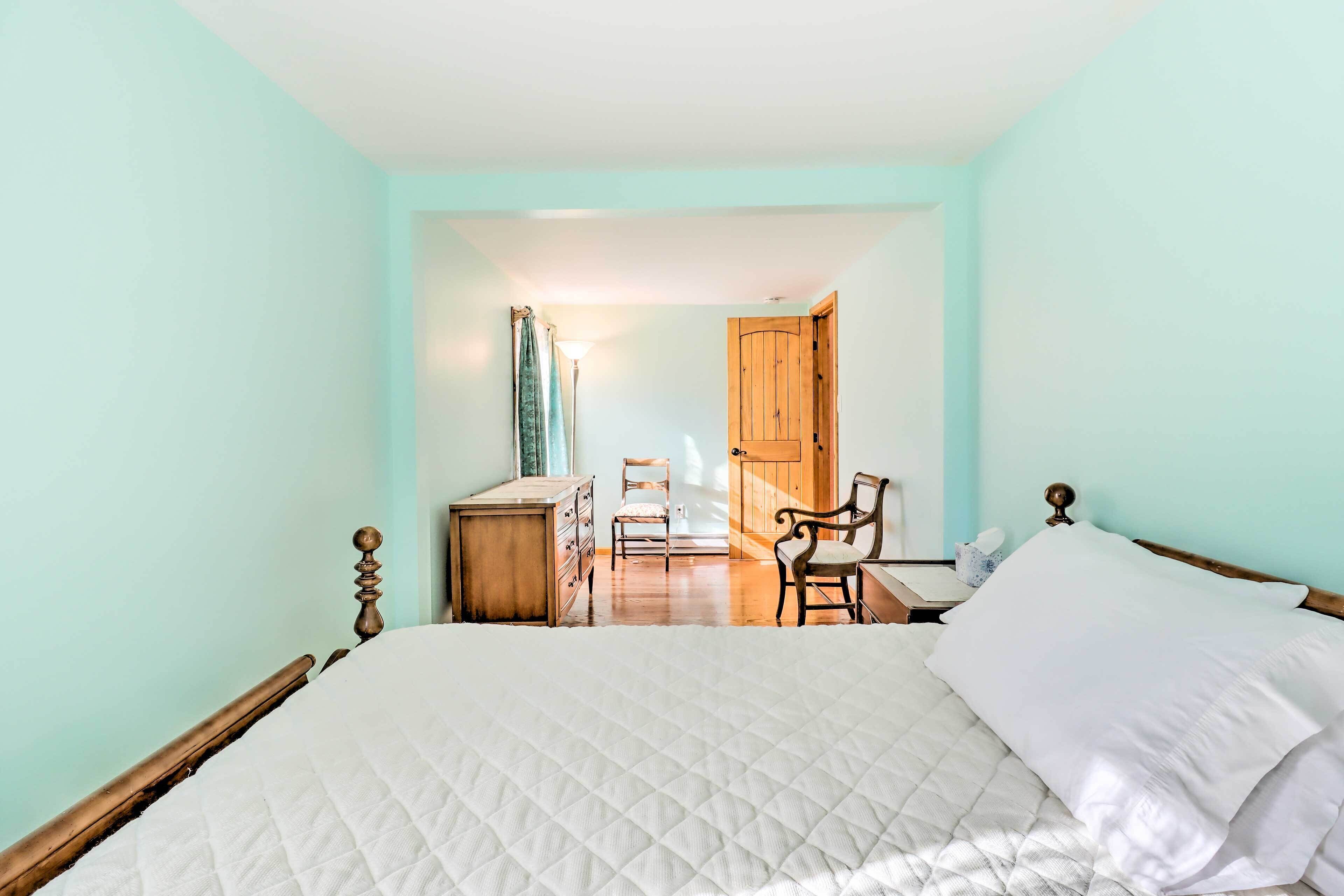 A bedroom with a large bed, wooden headboard, a dresser, a chair, and a desk with a lamp.