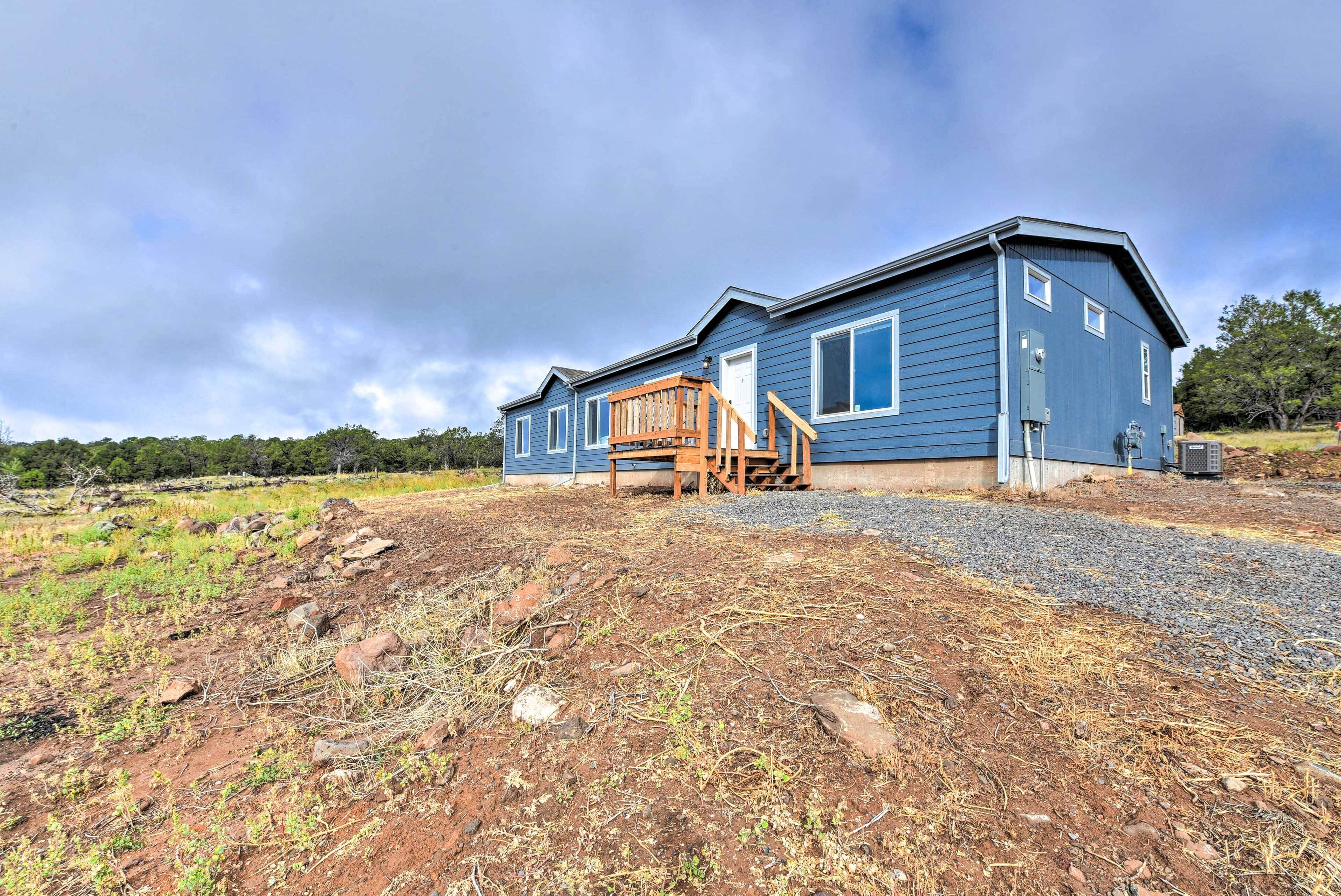 A two-story blue house with a wooden deck and a gravel driveway.