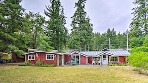 A red cabin with a covered patio, surrounded by a grassy yard and tall trees. - Wheelchair-accessible Belfair Cabin w/ Patio! (Belfair)