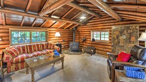 A log cabin interior with a wooden ceiling, a sofa, a table, a fireplace, and a window. - Wheelchair-accessible Belfair Cabin w/ Patio! (Belfair)