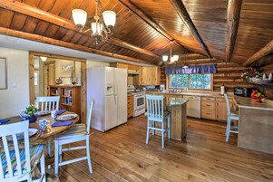 Una cocina rústica con pisos de madera, armarios blancos y una zona de comedor con sillas a rayas.