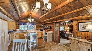 A rustic cabin interior with a wooden ceiling, a dining area with a table and chairs, a kitchen with wooden cabinets, and a cozy living area with a fireplace. - Wheelchair-accessible Belfair Cabin w/ Patio! (Belfair)