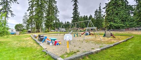 A playground with swings, slides, and a basketball hoop surrounded by trees.