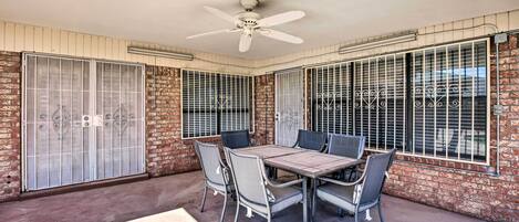 A covered patio area with a table and chairs, a ceiling fan, and barred windows.