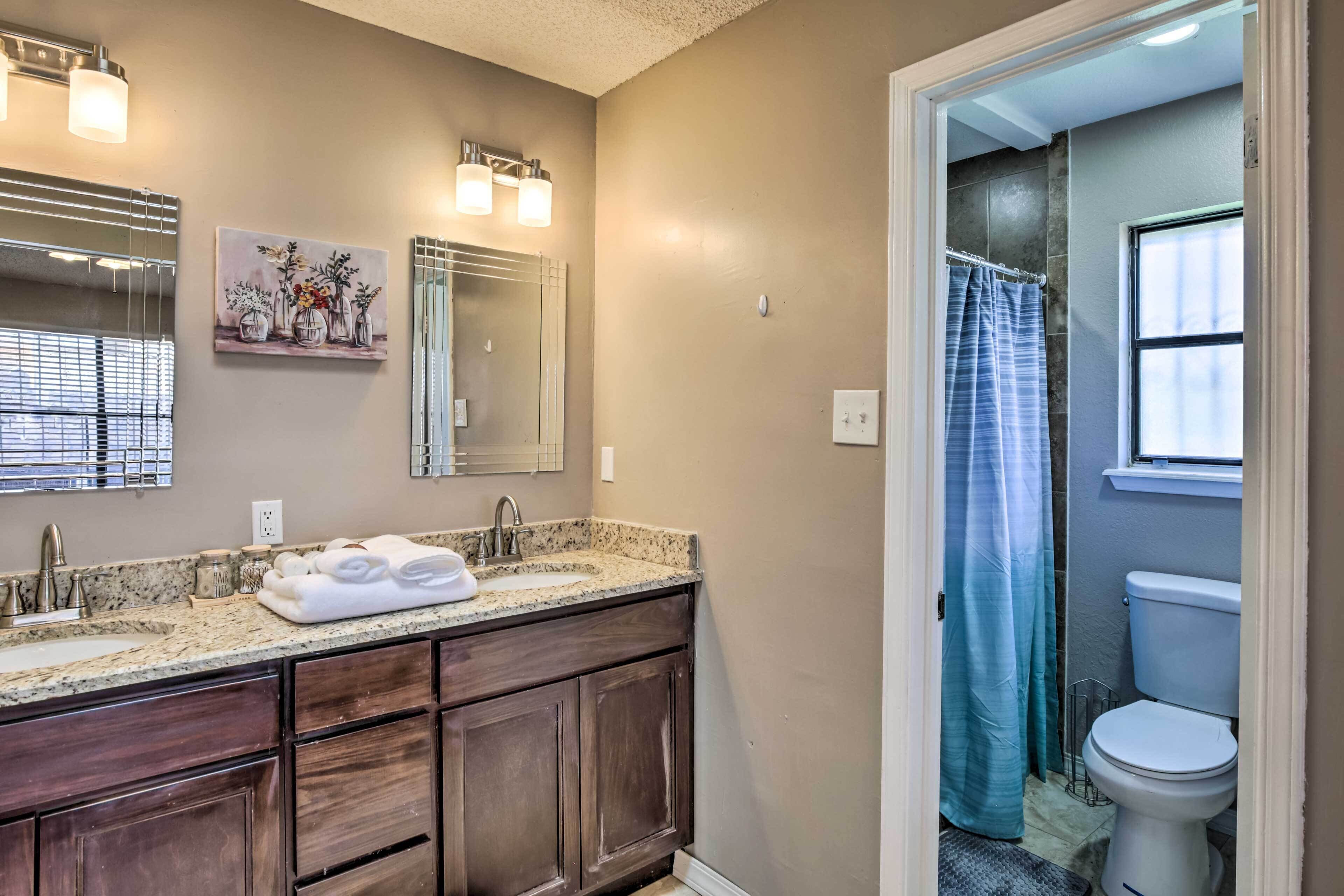 A bathroom with a granite countertop sink, dark wooden cabinets, a large mirror, and a shower curtain.