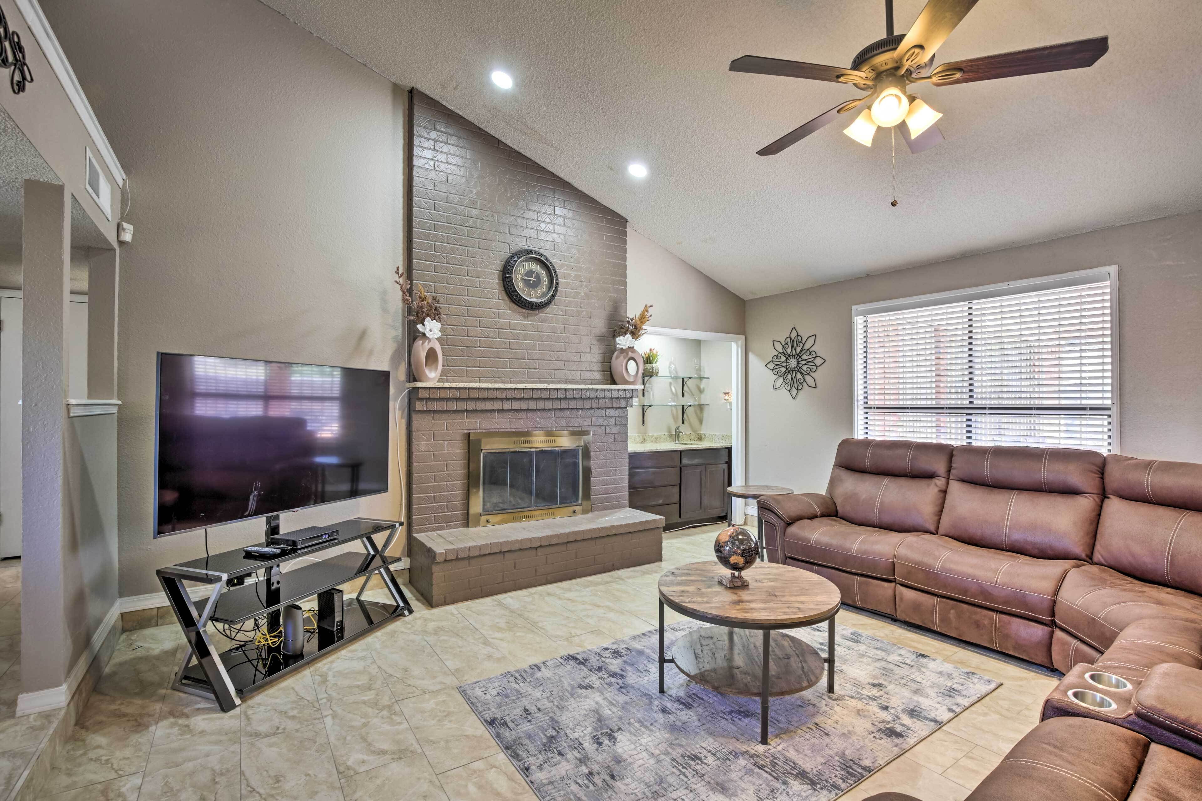 A living room with a TV, fireplace, leather sofa, and a ceiling fan.