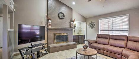 A living room with a TV, fireplace, leather sofa, and a ceiling fan.