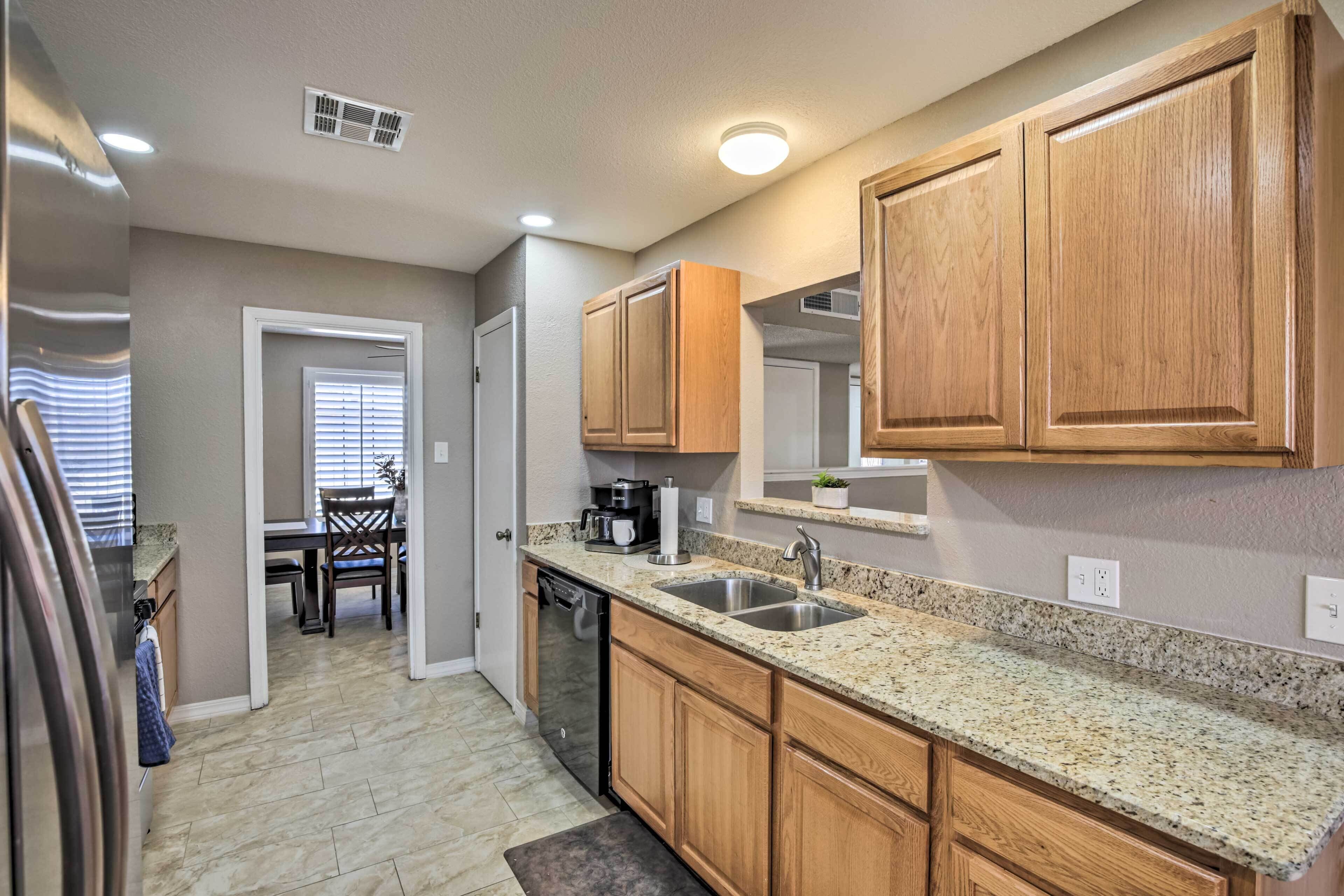 A kitchen with wooden cabinets, granite countertops, a dishwasher, and a dining area with a table and chairs.