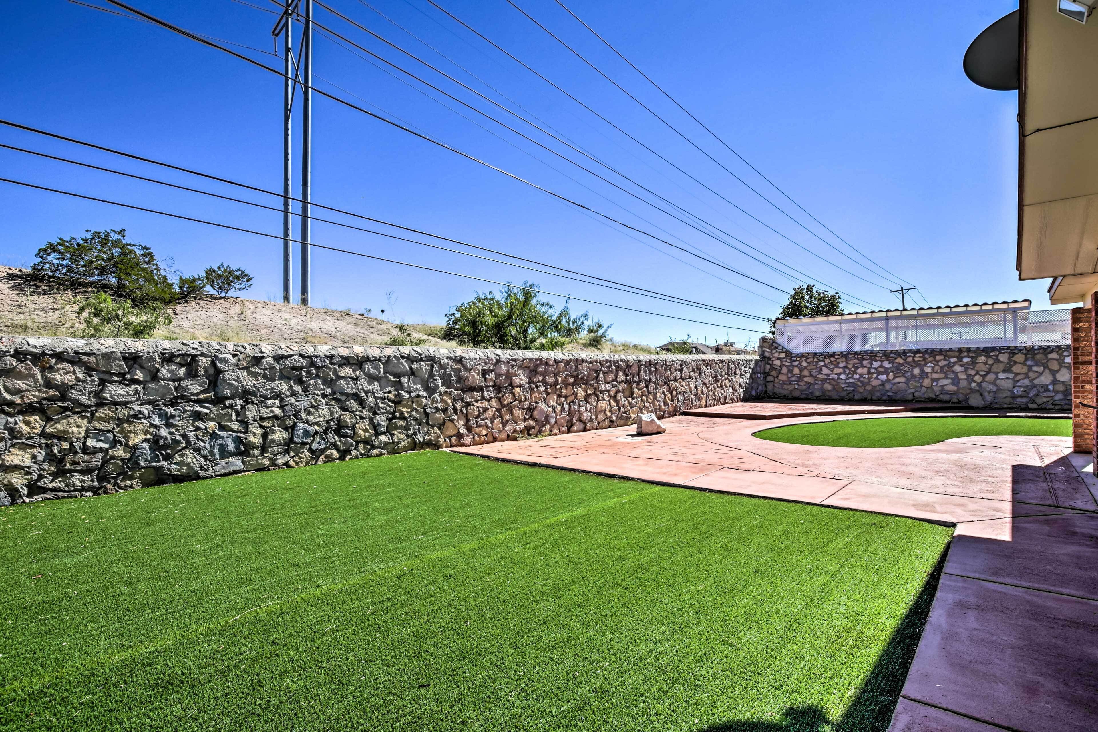 A landscaped backyard with a stone wall, a paved patio, and a well-maintained lawn.