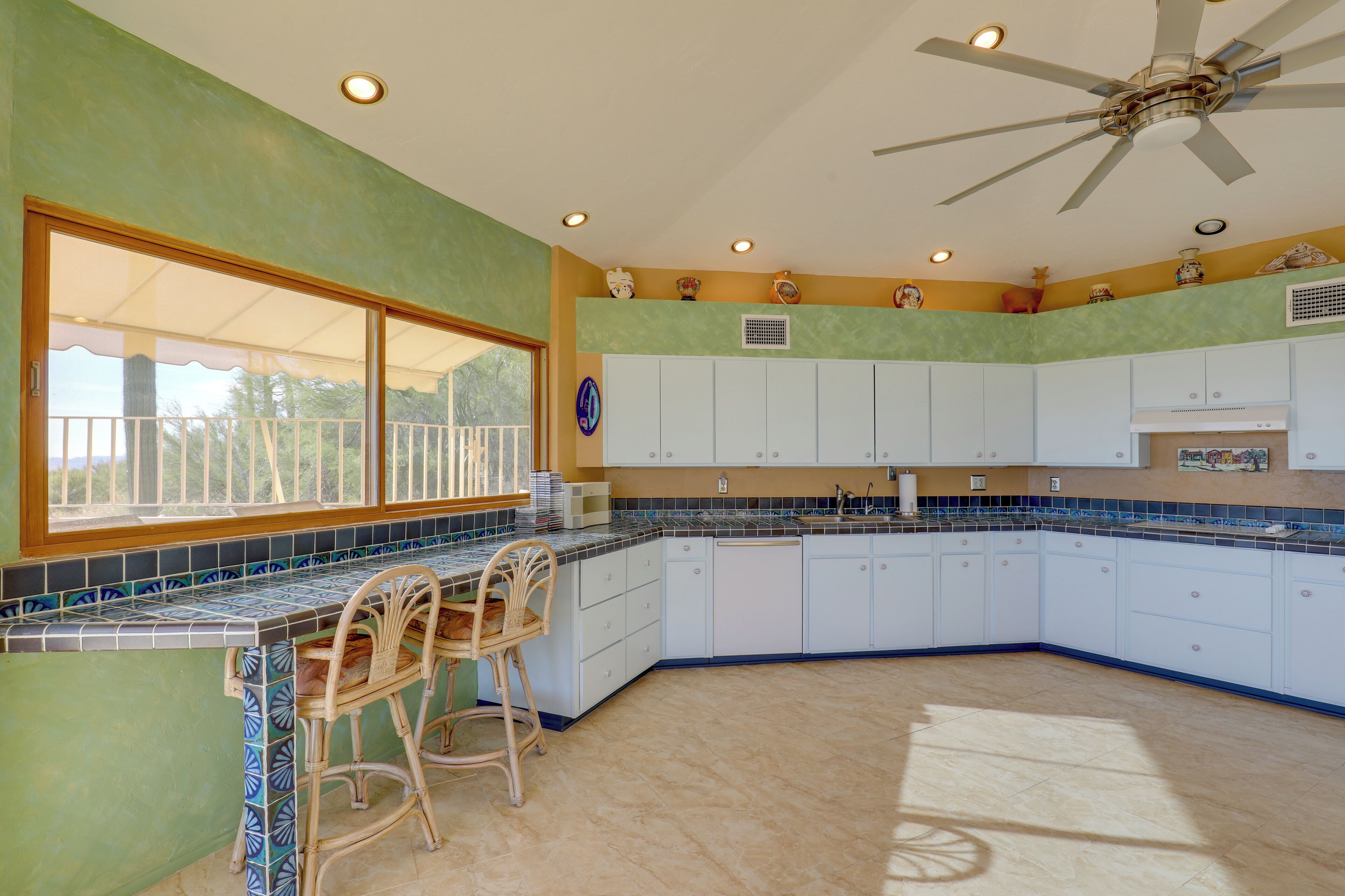 A kitchen with a large window, white cabinets, and a ceiling fan.