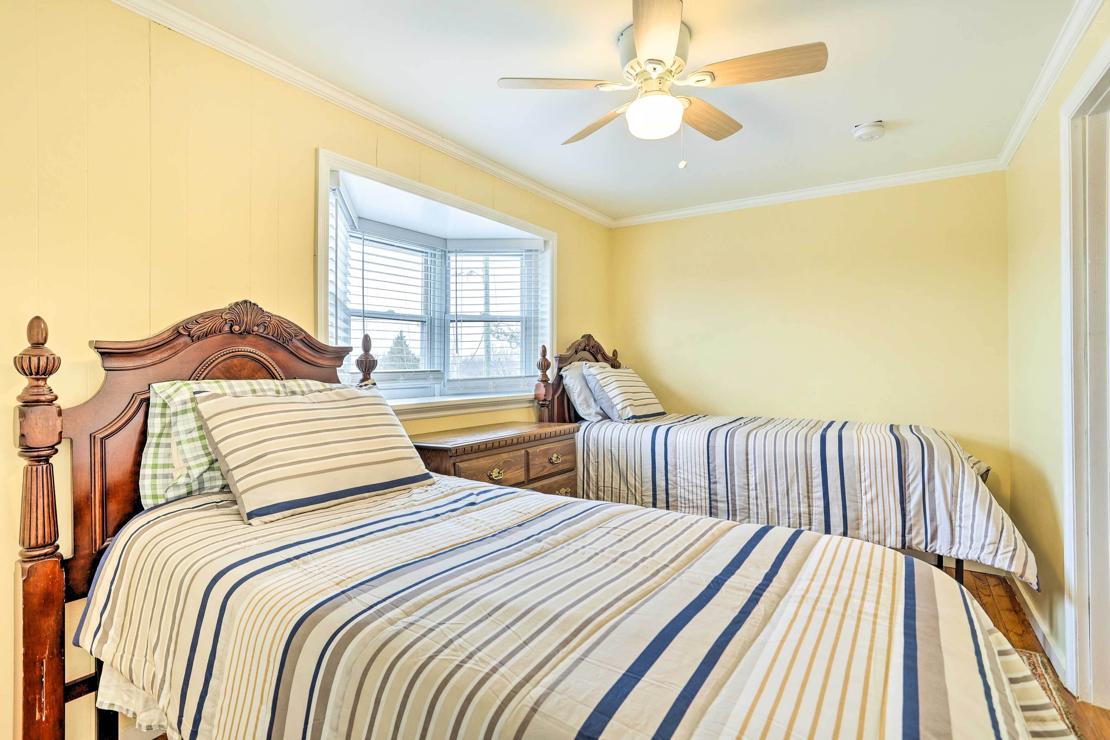 A bedroom with two beds, a wooden headboard, a nightstand, and a window with blinds.
