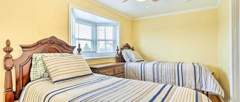 A bedroom with two beds, a wooden headboard, a nightstand, and a window with blinds.