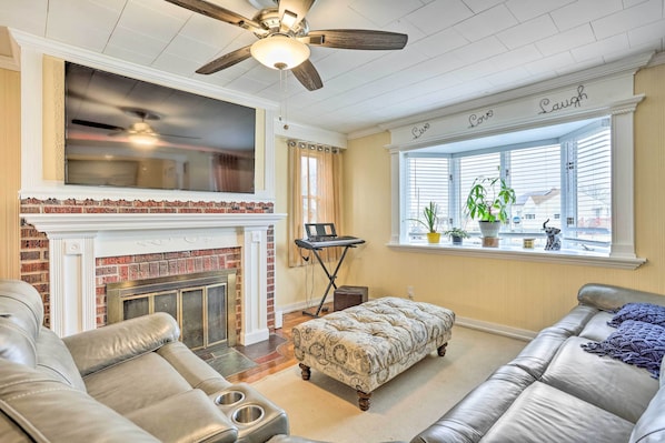A living room with a fireplace, leather sofas, a ceiling fan, and a window with a view. - Family Getaway Near Delaware River & Intl Soccer! (Gibbstown)