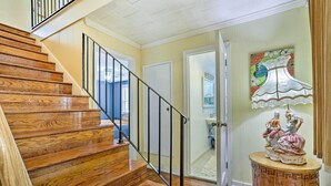 Uma escada de madeira com corrimão preto leva a um quarto com uma porta e uma mesa decorativa.