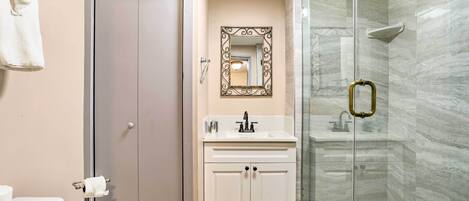 Un baño con inodoro, lavamanos con espejo y ducha con mampara de vidrio.