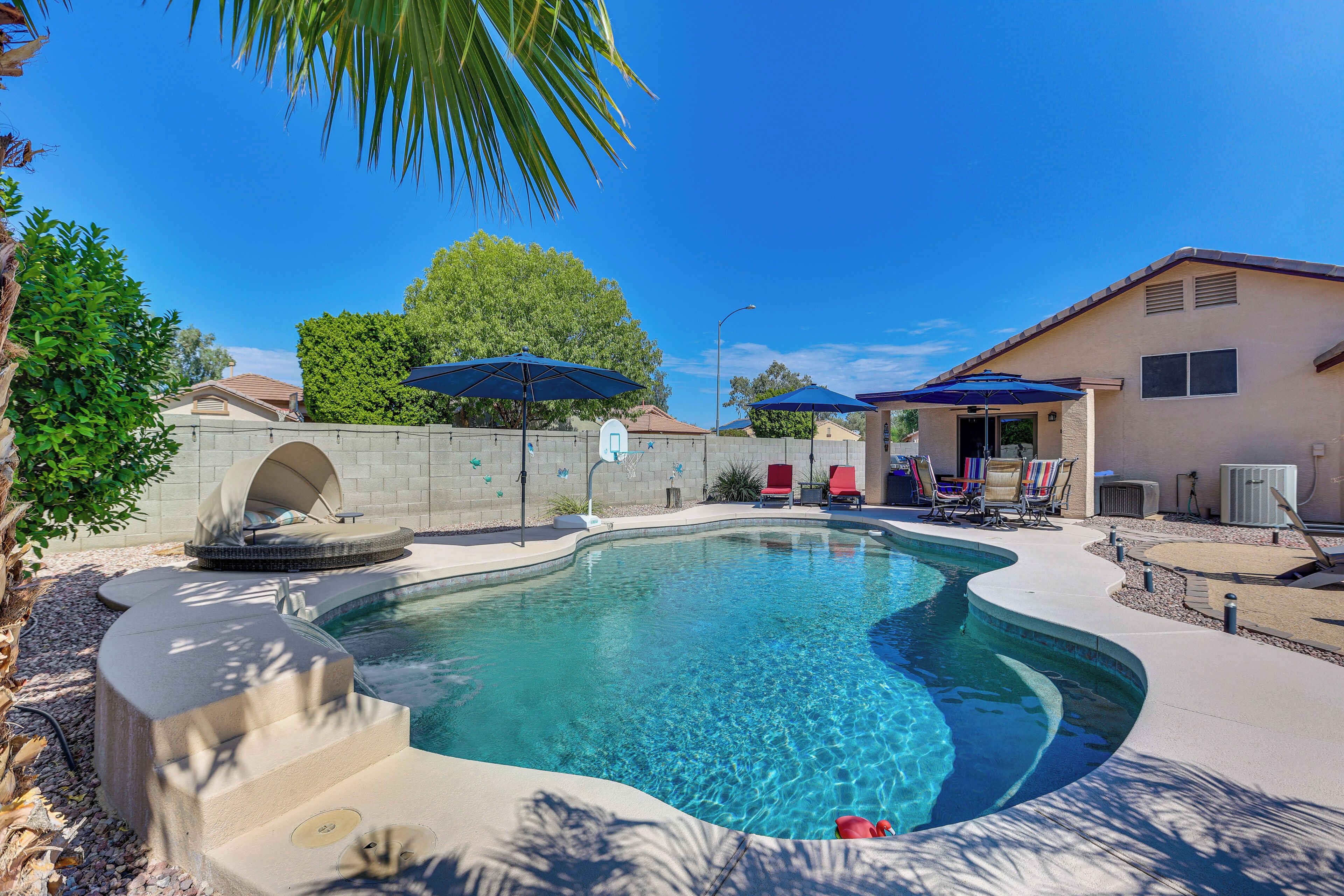 Une piscine à bord incurvé, entourée d’une terrasse en béton et ombragée par des parasols.
