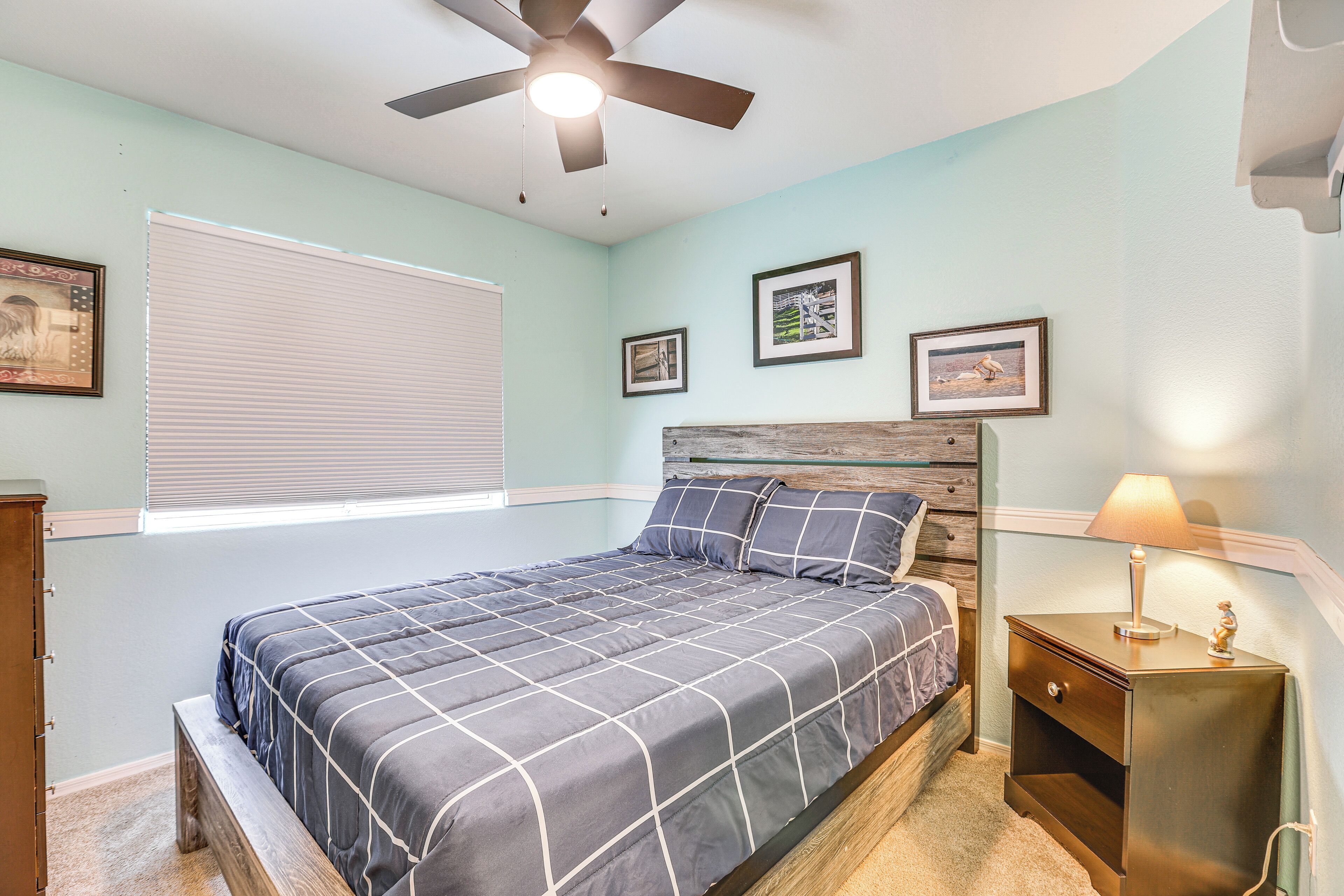 A bedroom with a bed, a nightstand, a ceiling fan, and a window with blinds.