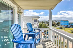 Un balcon avec deux fauteuils Adirondack bleus, une balustrade blanche et une vue sur les maisons voisines.