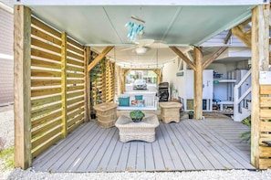 A covered outdoor deck with a ceiling fan, wicker furniture, and a view of a house in the background. - Coastal Oasis w/ Decks: Walk to Holden Beach! (Supply)