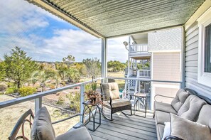 Une terrasse extérieure couverte, aménagée avec un canapé, un fauteuil et un pot de fleurs suspendu.