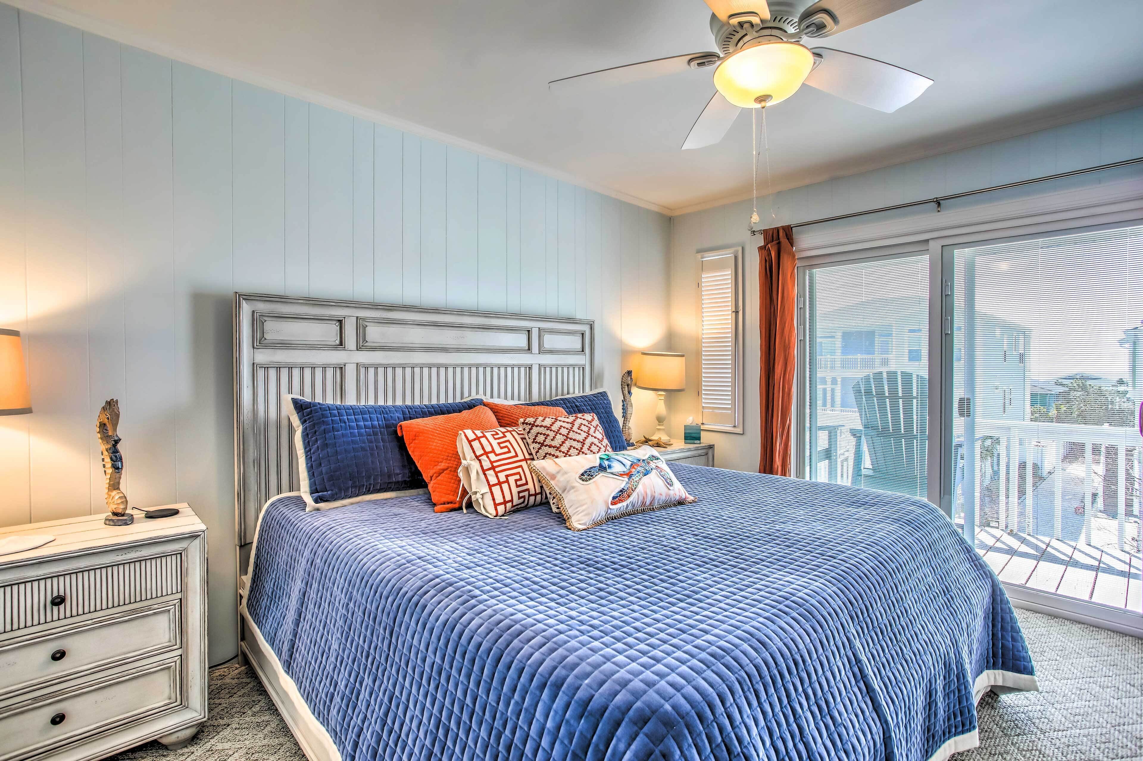 A bedroom with a large bed, a ceiling fan, and a view of the outside.