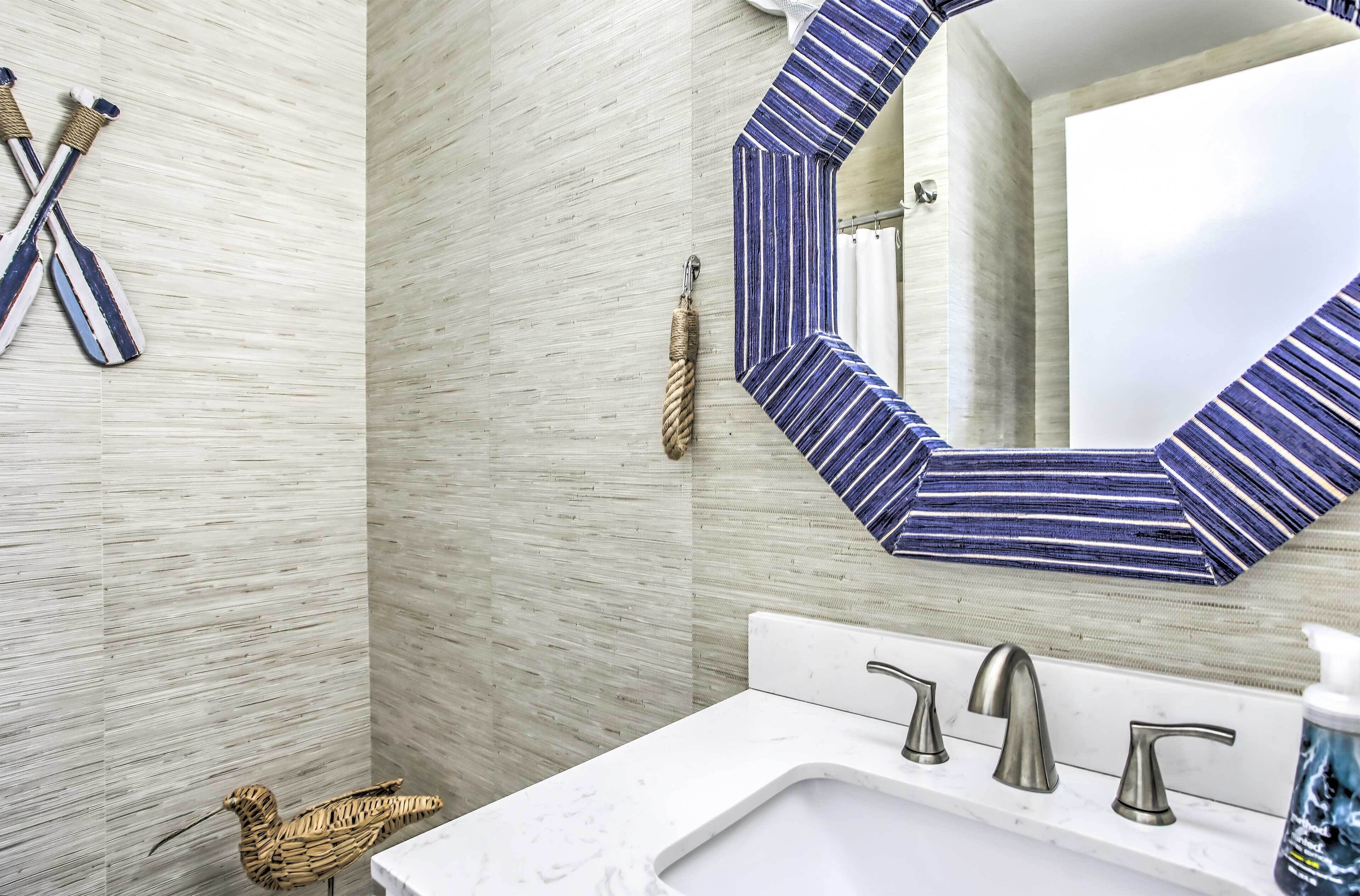 Ein Badezimmer mit einem weißen Waschbecken, drei Wasserhähnen, einem gestreiften Spiegel und einer Vogel-Skulptur aus Holz.