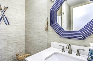 Ein Badezimmer mit einem weißen Waschbecken, drei Wasserhähnen, einem gestreiften Spiegel und einer Vogel-Skulptur aus Holz.