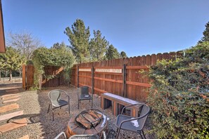 A backyard with a fire pit, two chairs, a bench, and a wooden fence.