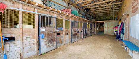 A stable with wooden stalls, metal gates, and hay bales.