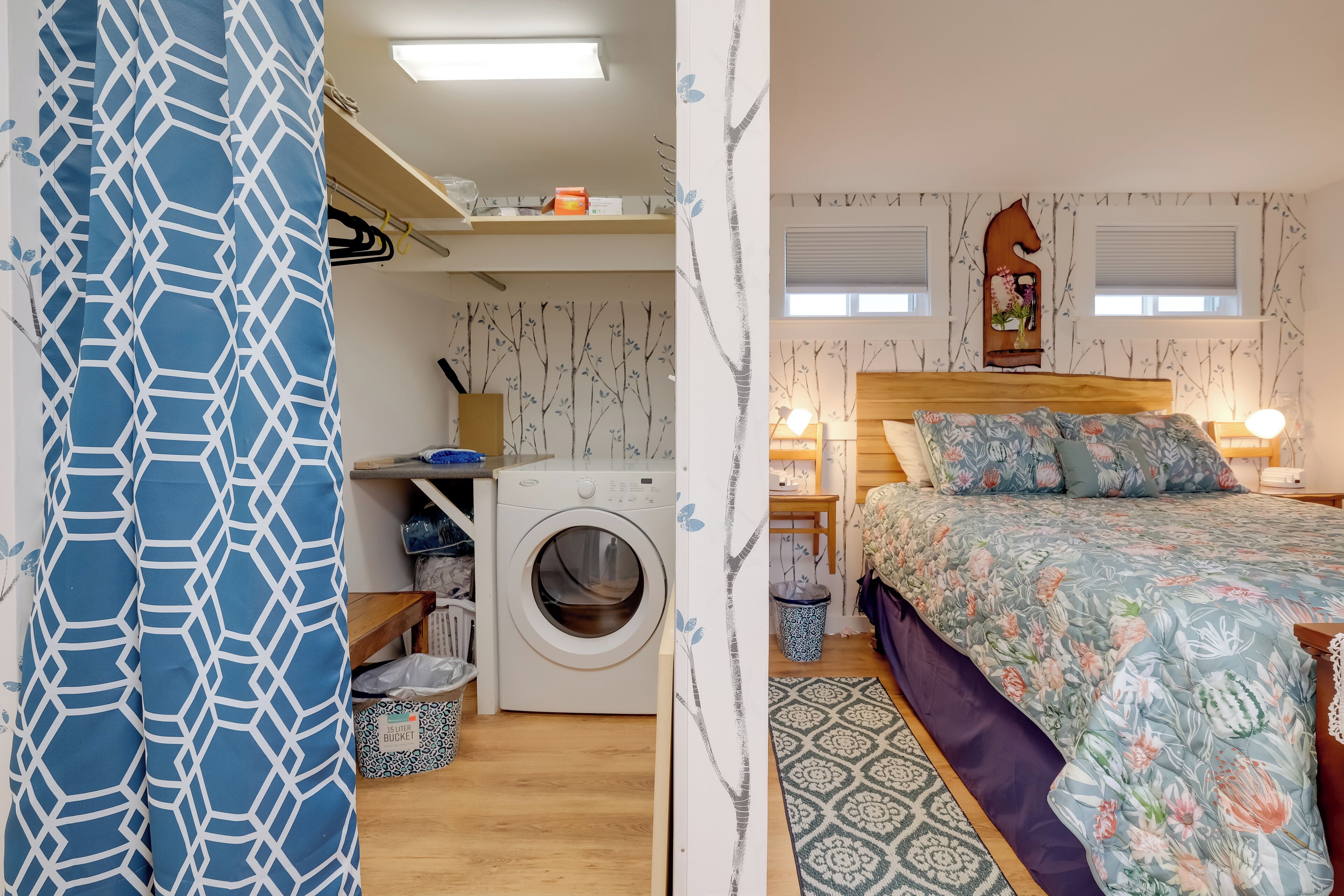 A bedroom with a bed, a washing machine, a shelf with items, and a window.
