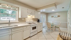 A kitchen with white cabinets, a stove, and a sink. There is a dining area with a table and chairs. - Waterfront Foley Area Home - 15 Mi to Gulf! (Elberta)
