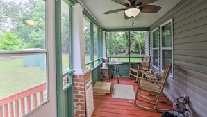 A covered porch with a ceiling fan, rocking chairs, a small table, and a view of the backyard.