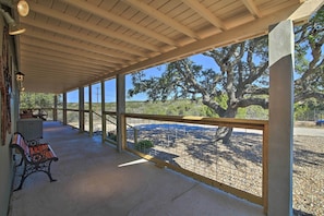 Un espace extérieur abrité, doté d’un banc, d’une table et offrant une vue sur un grand arbre et le paysage environnant.