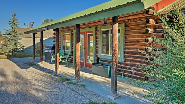 A log cabin with a porch, green chairs, and a gravel driveway.